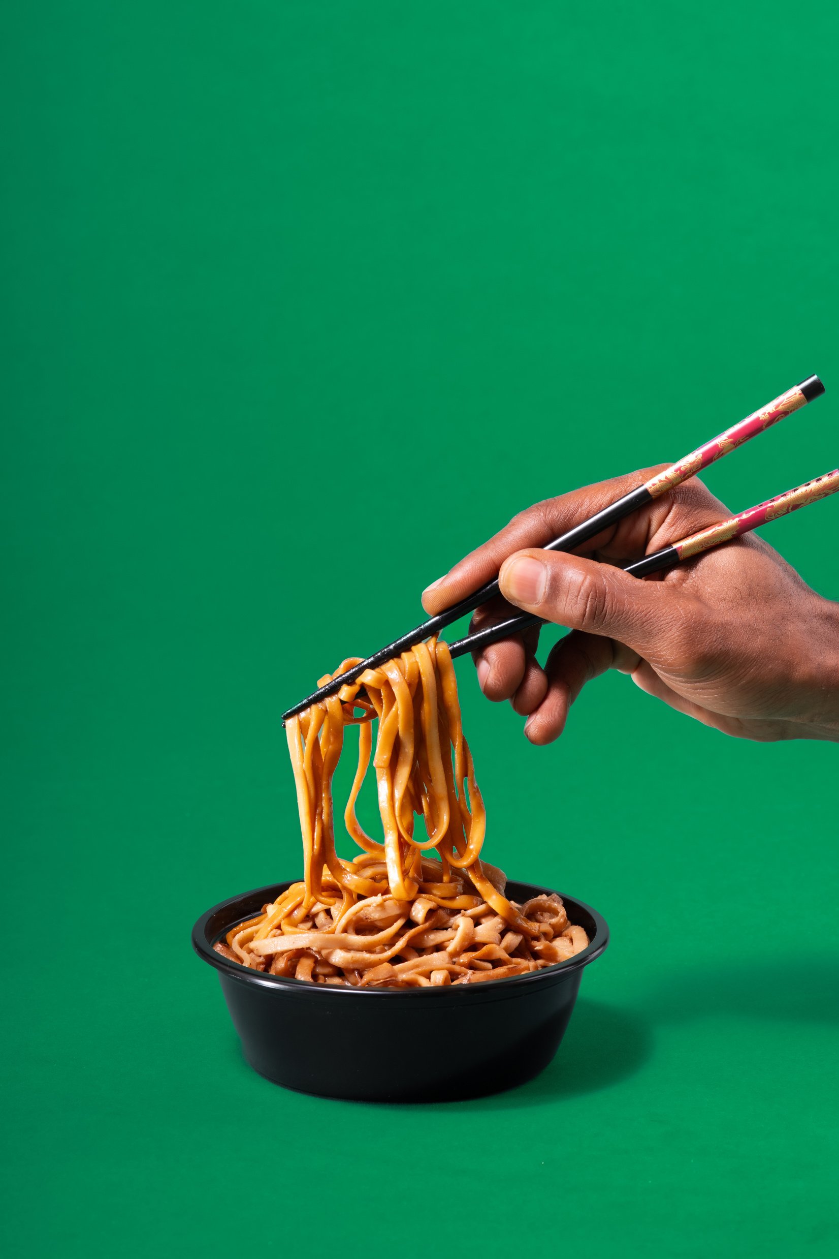 a hand holding chopsticks over a bowl of noodles