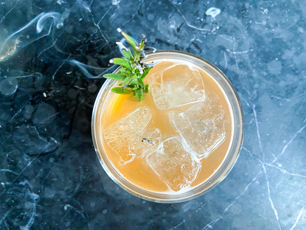 an orange drink with ice and a sprig of rosemary