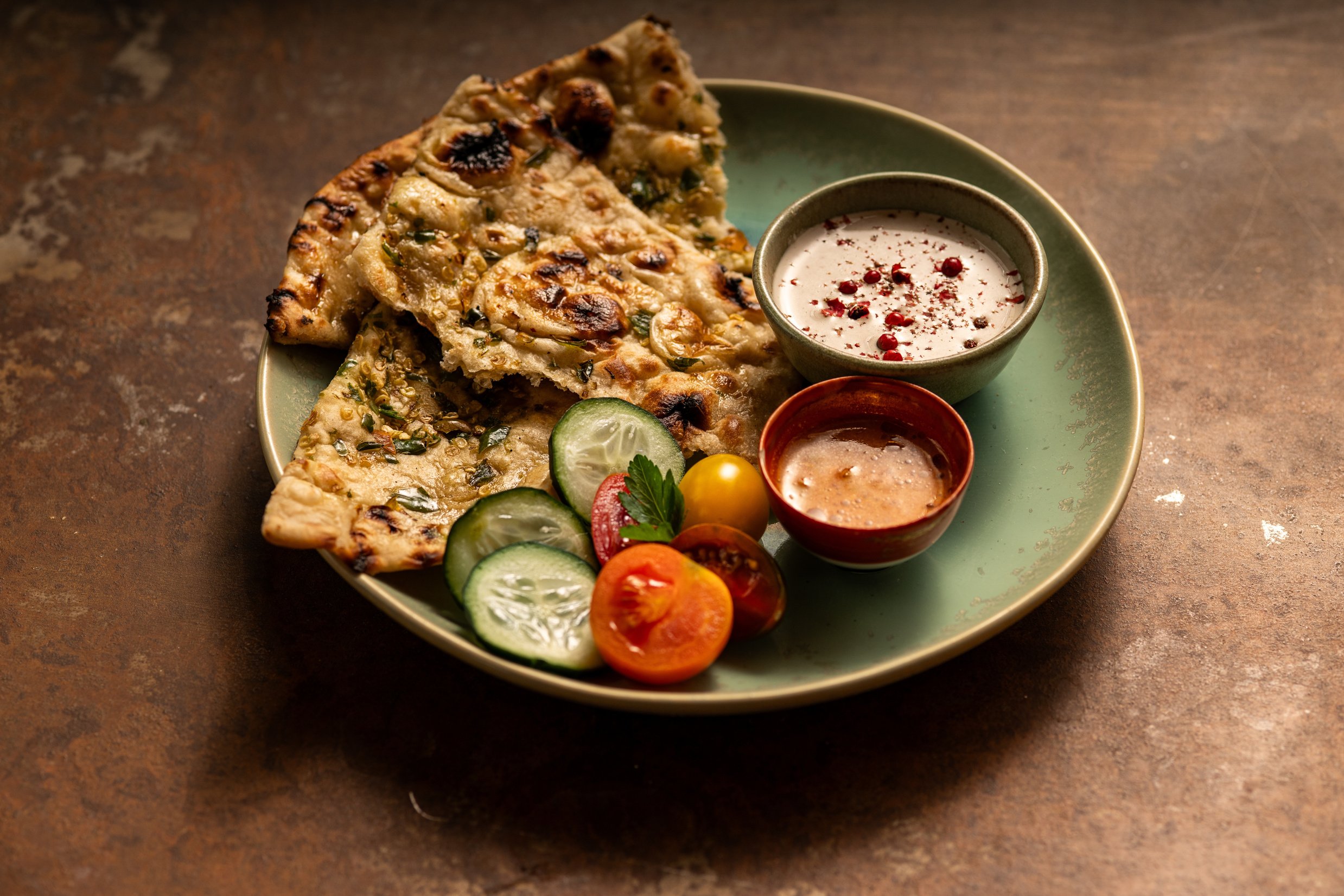 a green plate topped with flatbread, cucumbers and tomatoes