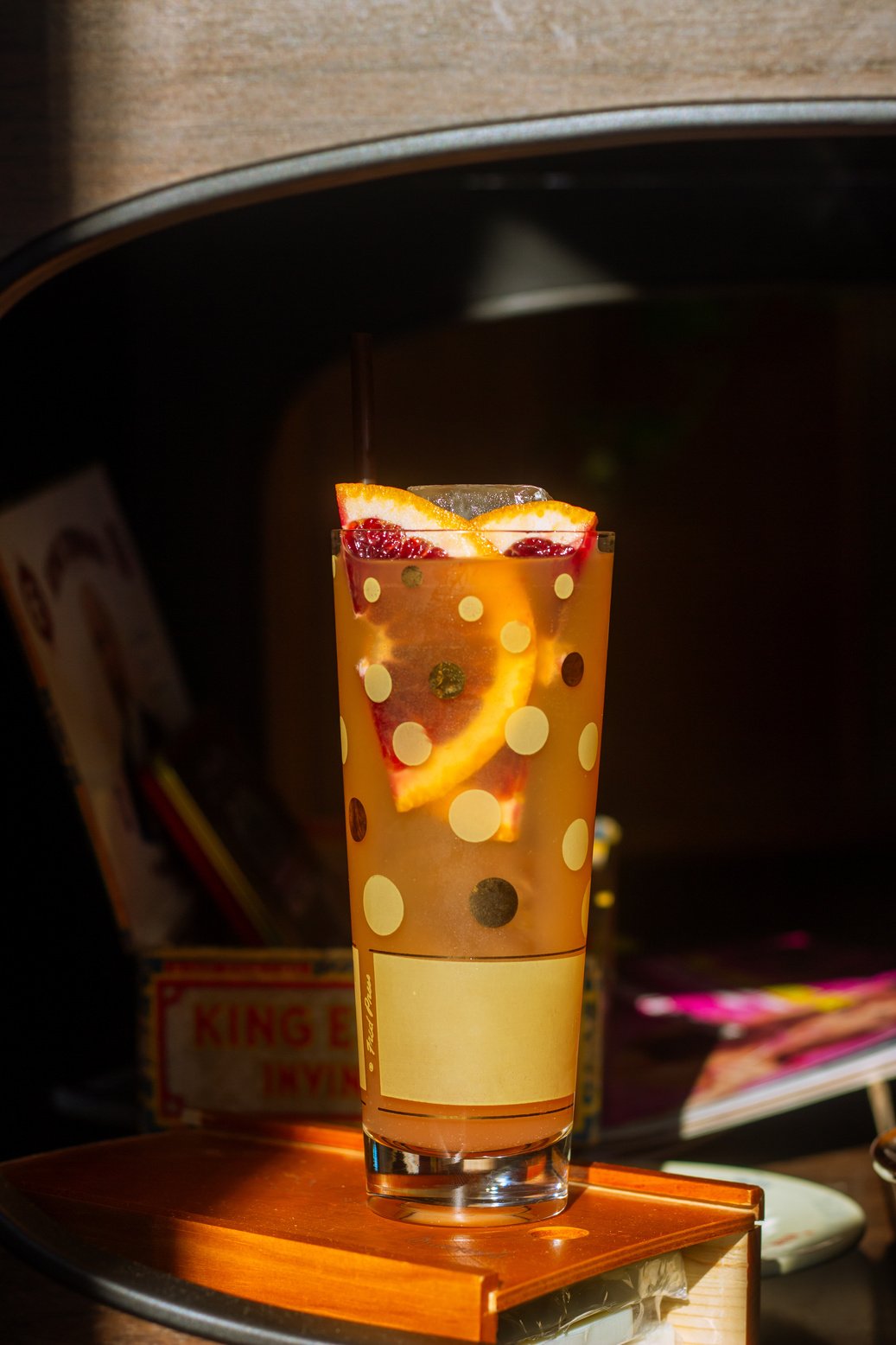 a cocktail with blood orange slices in a tall polka-dot glass