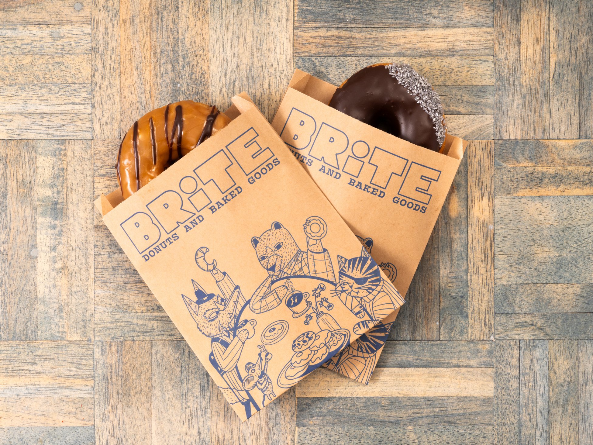 two donuts in brown paper bags on a wooden table